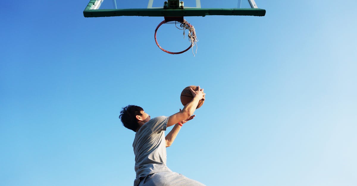 A young man jumping to dunk a basketball outdoors in clear daylight.