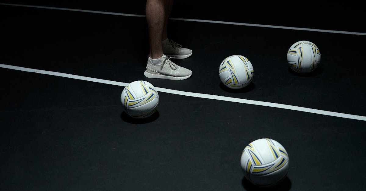 Person in sneakers with volleyballs on indoor court.