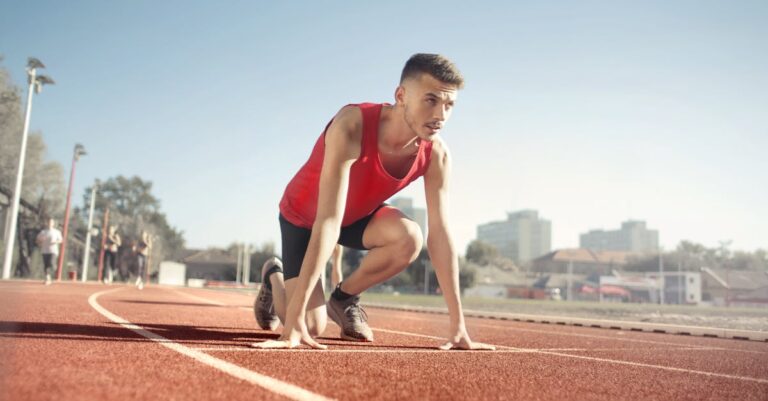 Young male athlete in start position on outdoor track, ready to sprint.