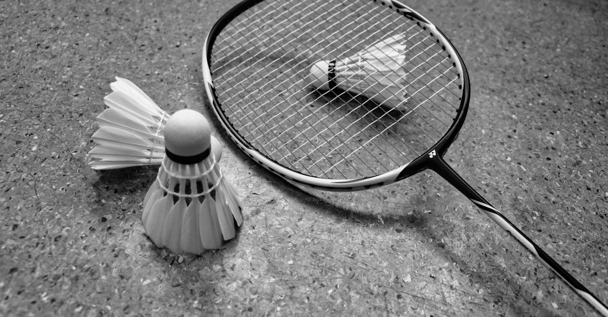 Grayscale image of badminton racket and shuttlecocks on a court surface.