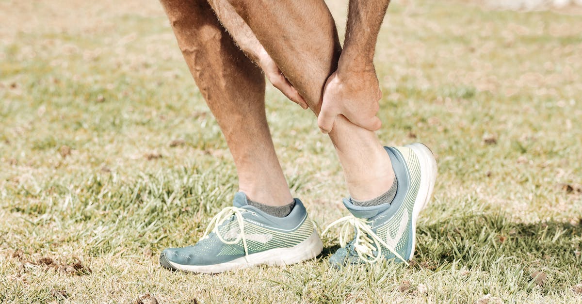 Man holding his calf in pain, wearing teal sneakers on green grass.