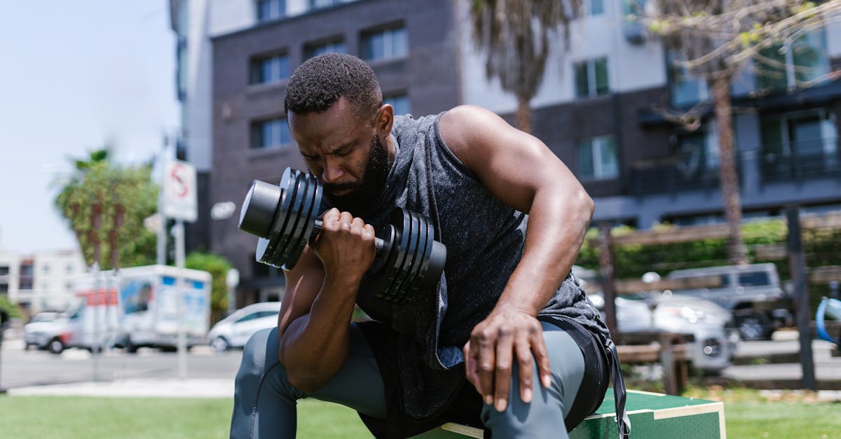 Focused man working out with dumbbell in a city park, showcasing fitness and concentration.