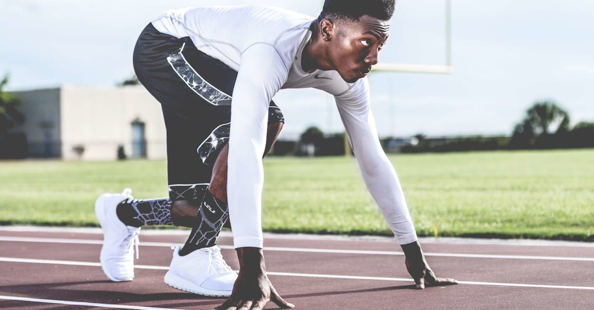 Focused athlete in starting position on a sunny track field, ready to sprint.