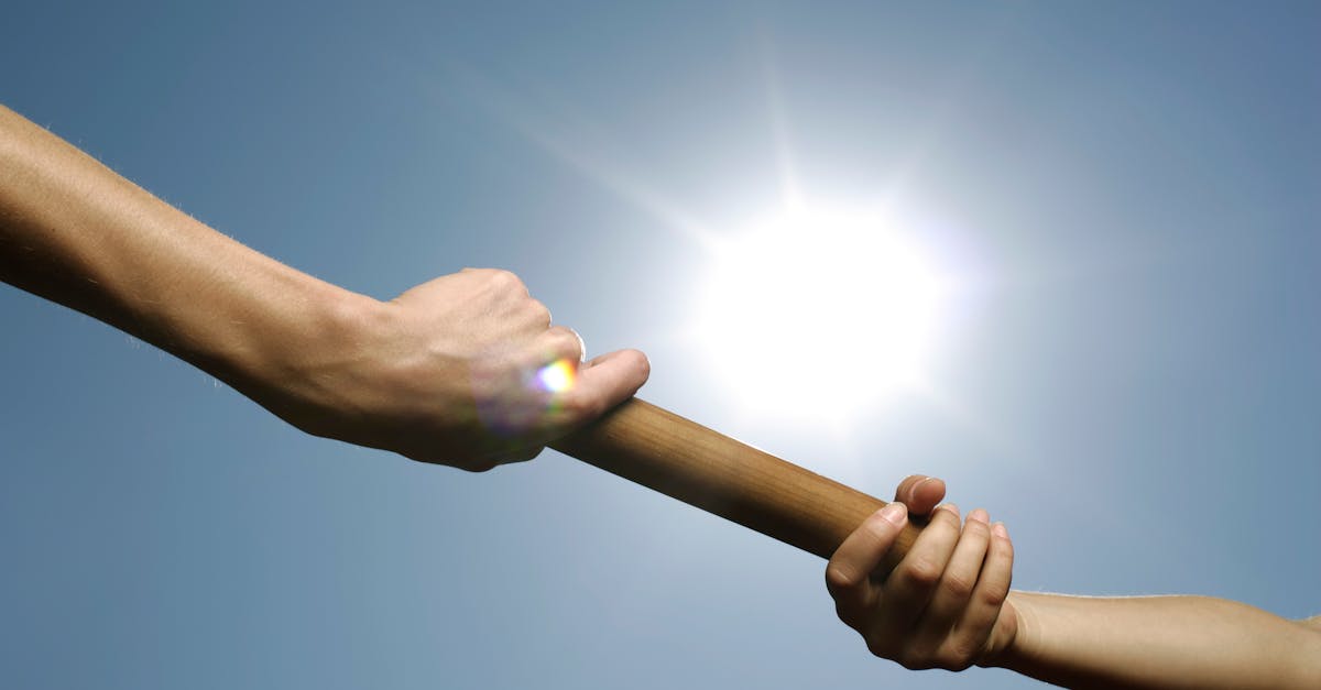 Close-up of hands passing a relay baton against a bright sunny sky. tongkat lari estafet, gambar tongkat lari estafet