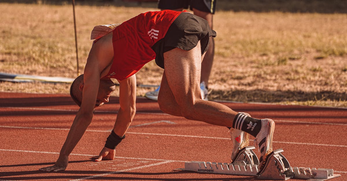 Athlete in red preparing to sprint on an outdoor track field. Focus on starting technique.