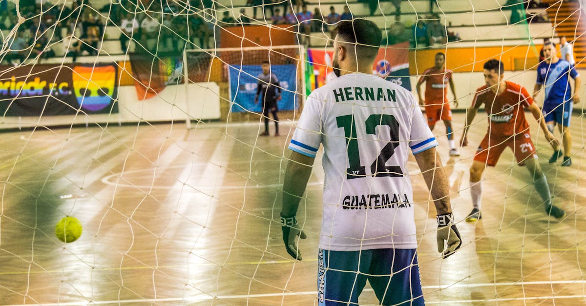 Goalkeeper watches incoming players in an intense indoor soccer match.