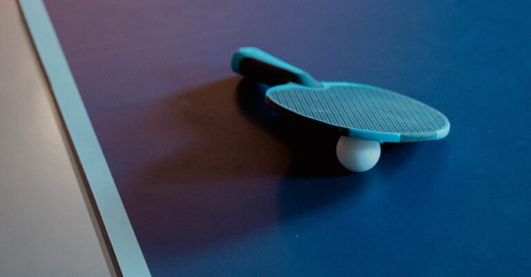 Close-up of a table tennis paddle and ball on a blue table, indoor setting.