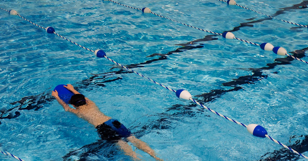 A young swimmer practicing with a kickboard in a swimming pool on a sunny day.