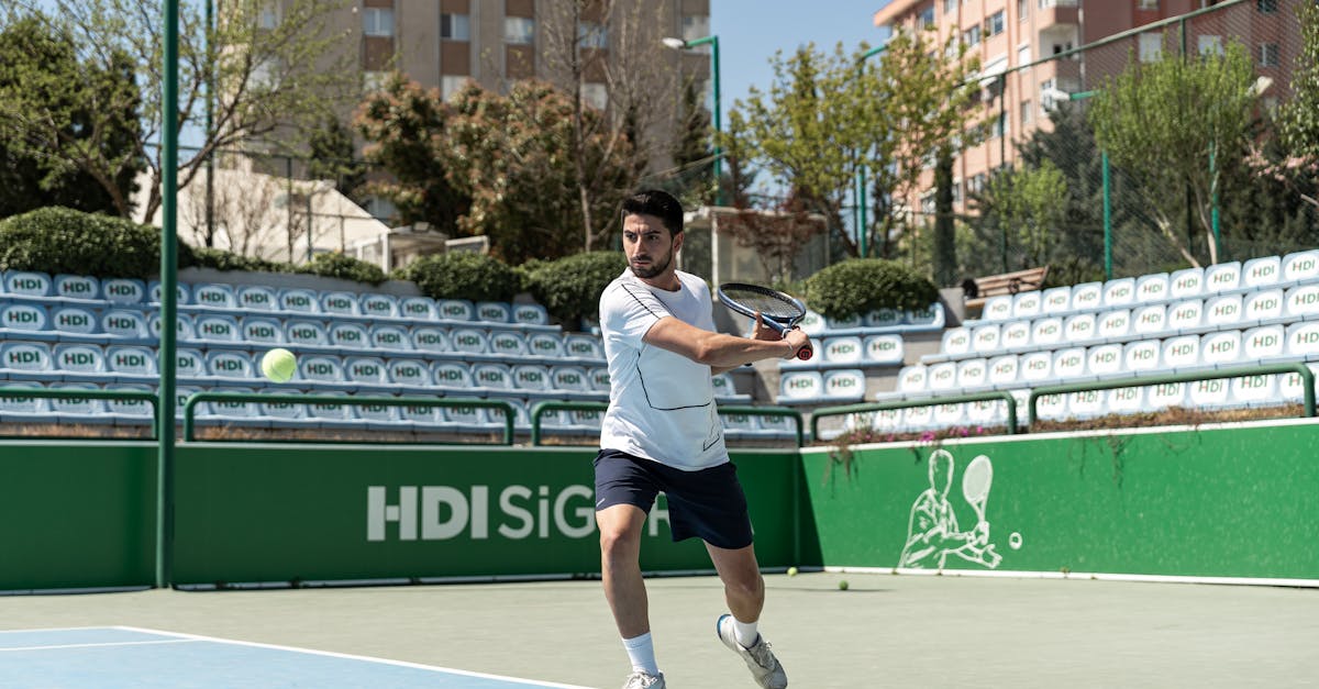 Male tennis player hitting a ball on an urban outdoor court during the day.