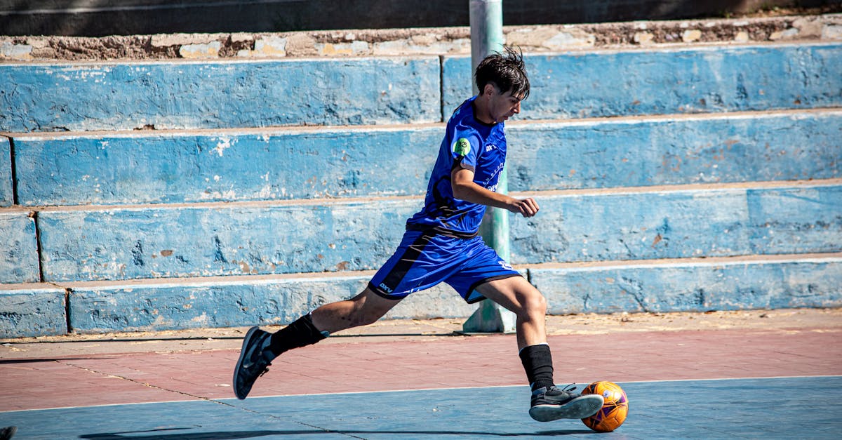 Teenage boy in blue jersey playing soccer on an outdoor court, mid-action.