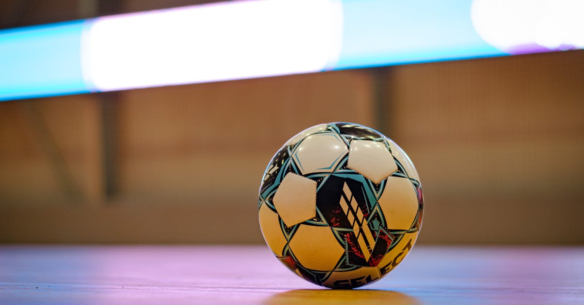 Close-up of a soccer ball on a gym floor with blurred background lights.