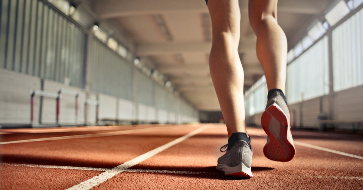 From below back view of crop strong runner walking along running track in athletics arena while doing warm up exercises during workout