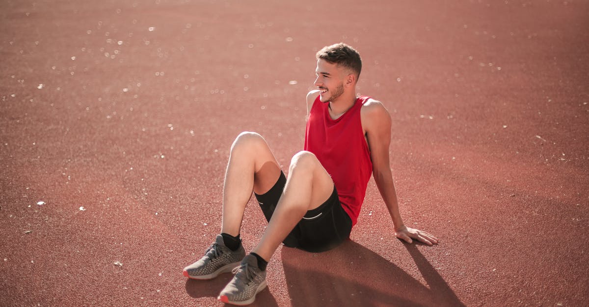 A young man in sportswear relaxing on an outdoor track field in daylight.