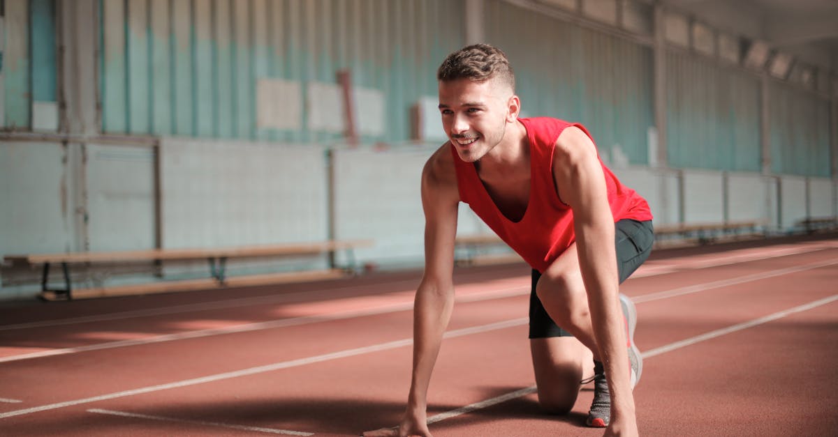 A young male athlete preparing to start running on an indoor track with a smile.