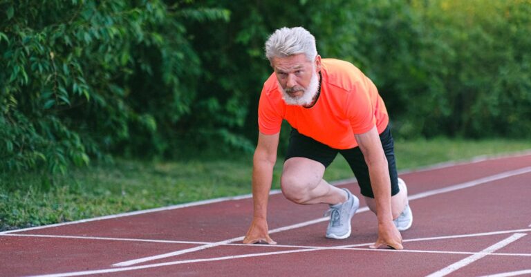 Elderly athlete in bright attire starts a sprint on an outdoor track, showcasing energy.