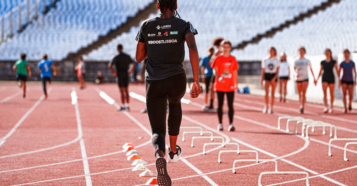 An athlete performing drills on an outdoor track in Lisbon with hurdles and cones.