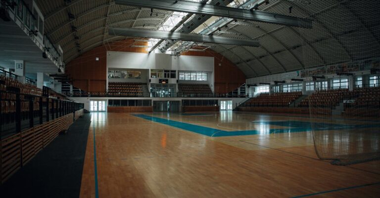 Empty indoor sports arena with hardwood flooring and bleachers, perfect for various sports activities.