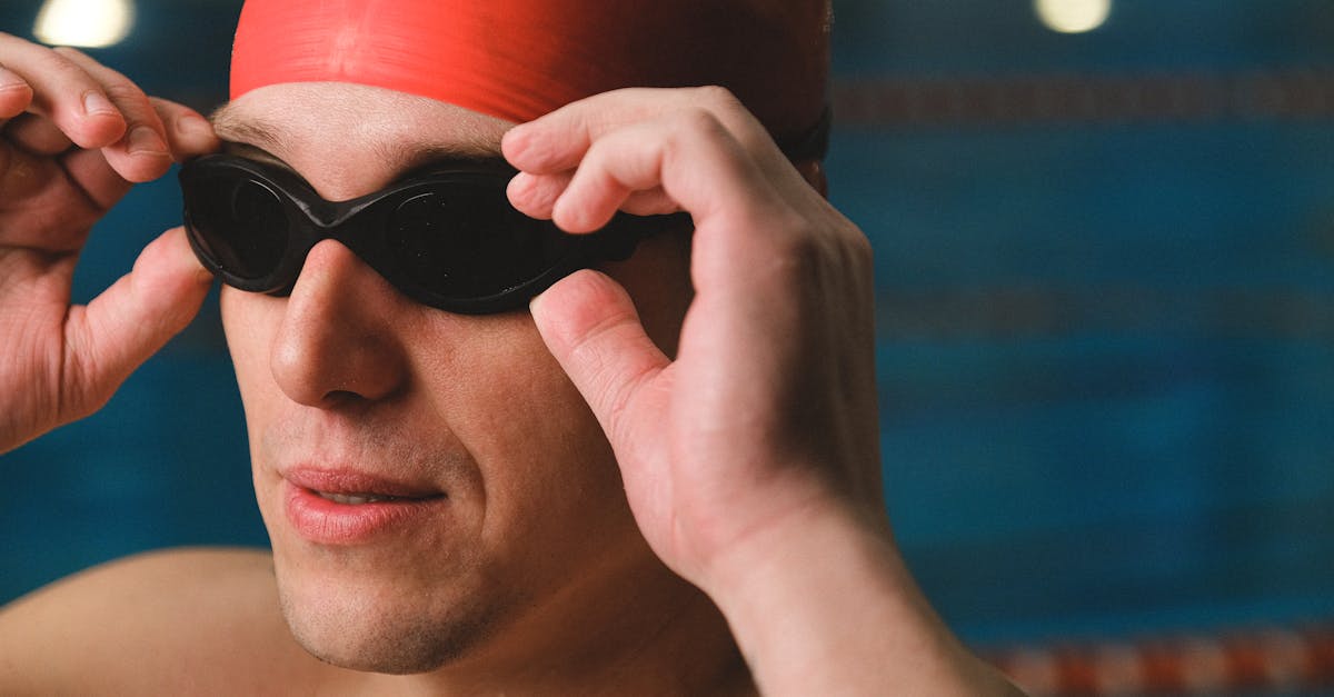 A male swimmer adjusts his goggles, focusing before a swim in an indoor pool.