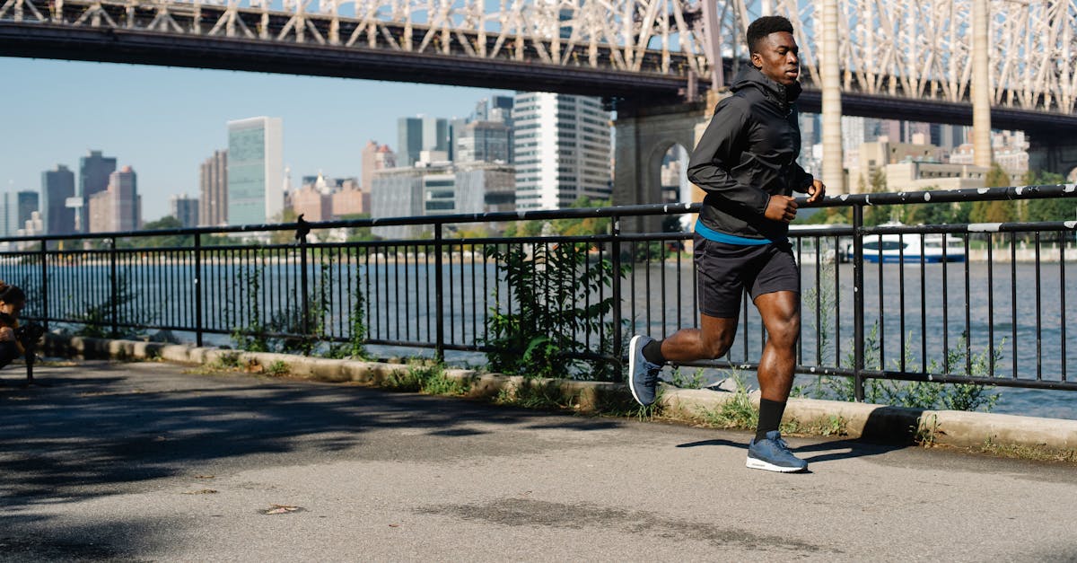 African American man jogging by the river with an urban bridge and city skyline in the background, promoting healthy living.