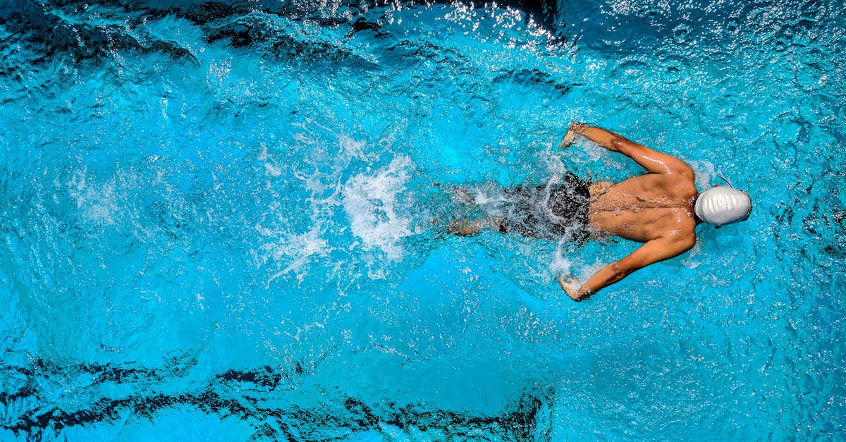 Top view of a swimmer wearing a cap, performing a front crawl stroke in a clear blue swimming pool.