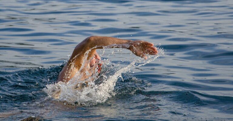 A male swimmer performing freestyle stroke in open water, creating splashes.